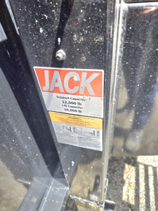 Trailer frame shows a Jack brand sticker with capacity details: support capacity 12,000 lb and lift capacity 10,000 lb on the gooseneck flatbed trailer.