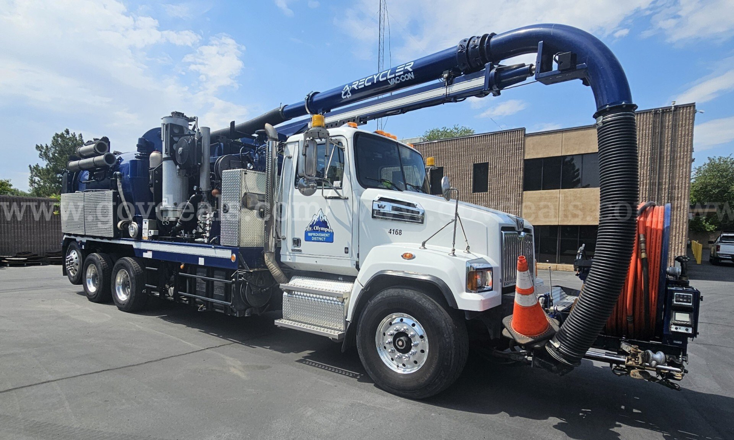 Large vacuum truck with a long blue boom and reel on the side, white cab, viewed from the front passenger side.