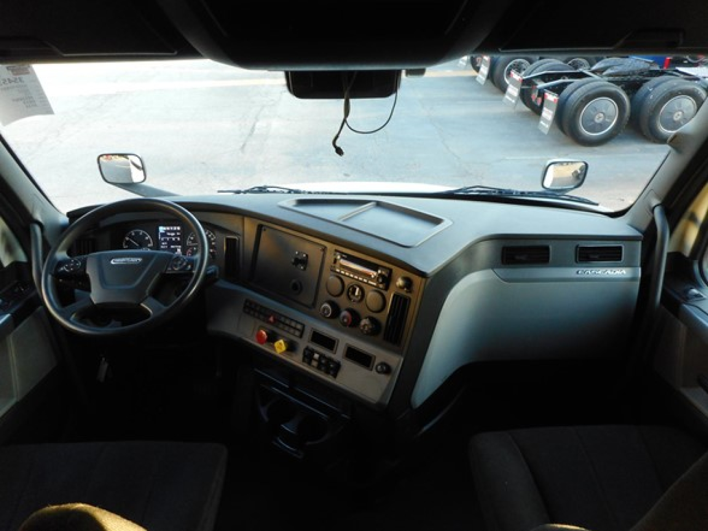 Truck cab interior dashboard view from driver seat in a Freightliner Cascadia 116 showing steering wheel, instrument cluster, and control panel.