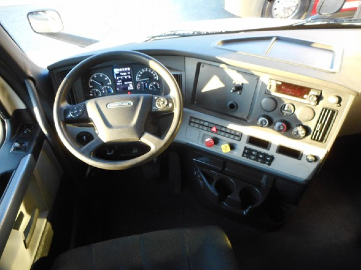 Truck cab interior shot showing steering wheel, dashboard, gauges, and center console of a Freightliner Cascadia-style truck.