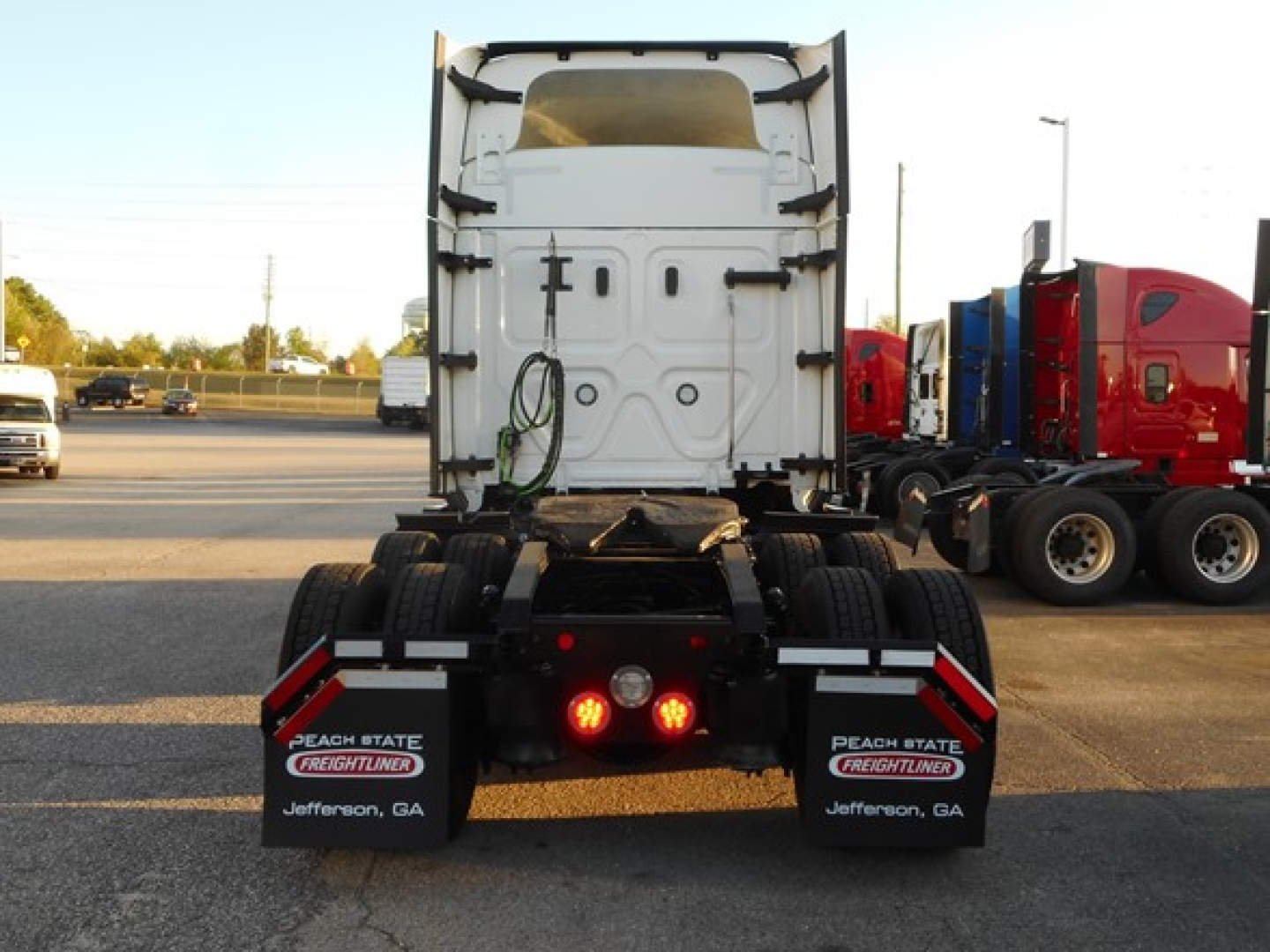 Rear view of 2022 Freightliner Cascadia 116 tractor showing dual rear mud flaps with Peach State Freightliner logos and Jefferson, GA, chassis with fifth wheel area and back lights visible.