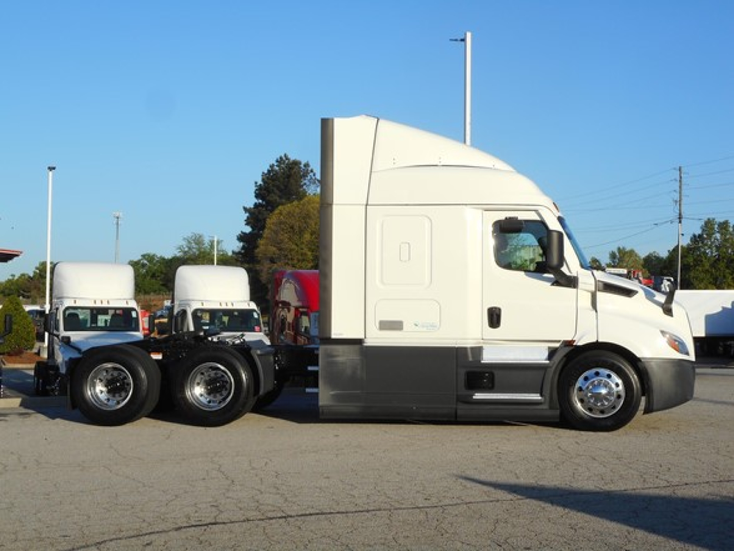Semi truck side view showing Freightliner Cascadia 116 sleeper with attached trailer chassis and wheels.