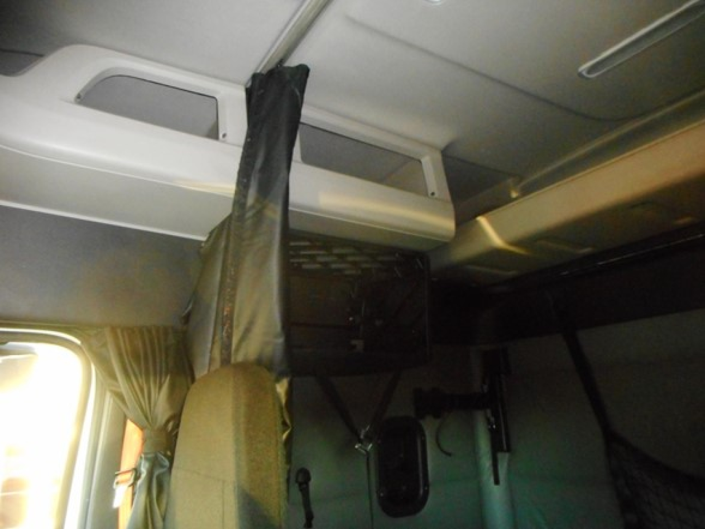Truck cab interior showing sleeper area with curtains and overhead storage hatch.