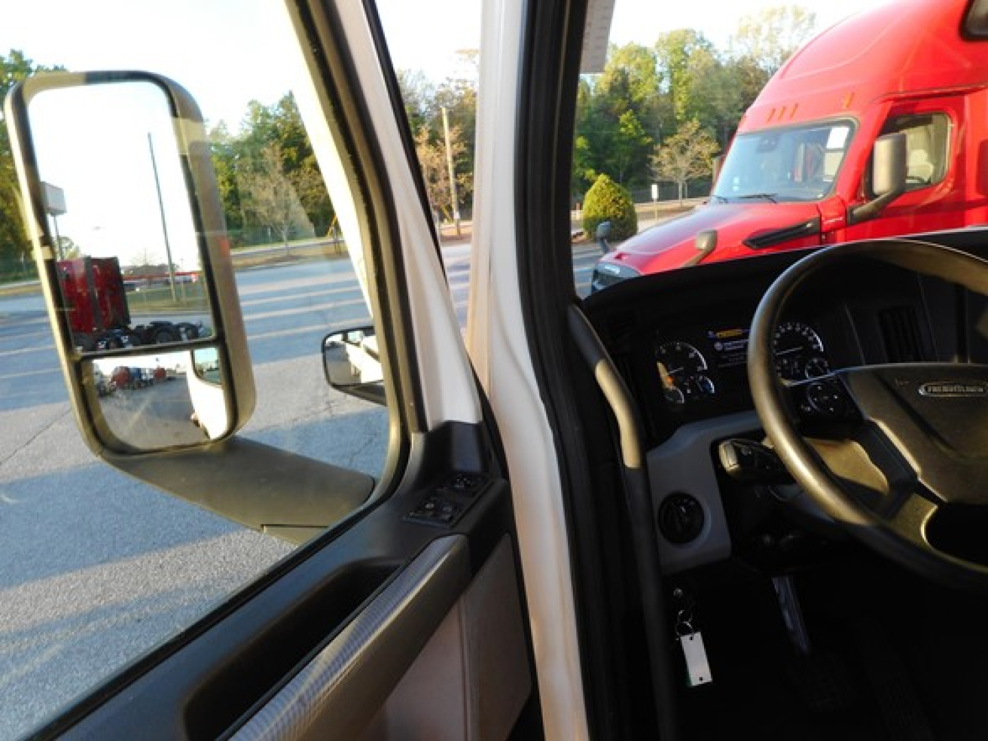 Freightliner Cascadia interior dashboard and steering wheel view from open cab door.