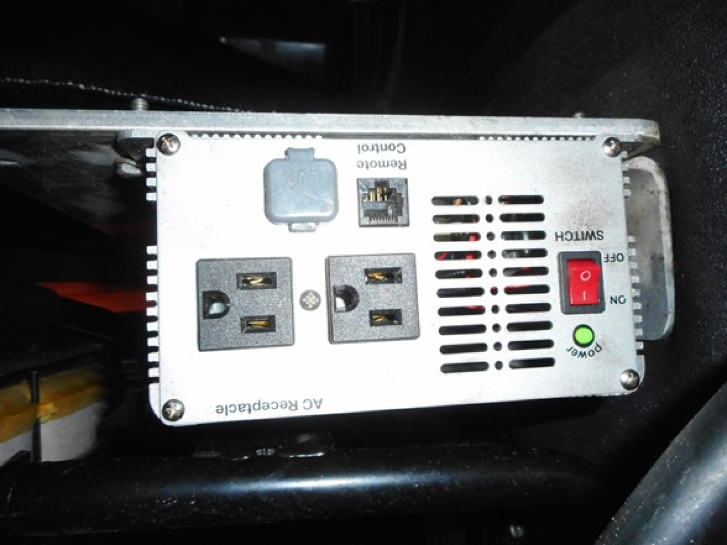 AC receptacle and control panel of a power inverter mounted in a Freightliner Cascadia engine bay showing AC receptacles, USB? No, two 120V outlets, ground fault switch, and control panel labels.