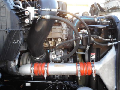 Engine bay of a 2022 Freightliner Cascadia 116 showing hoses, intercooler piping, and a red silicone hose with clamps across a metallic pipe.