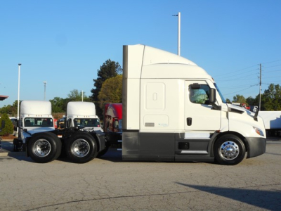 Semi truck side view showing Freightliner Cascadia 116 sleeper with attached trailer chassis and wheels.