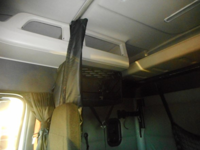 Truck cab interior showing sleeper area with curtains and overhead storage hatch.