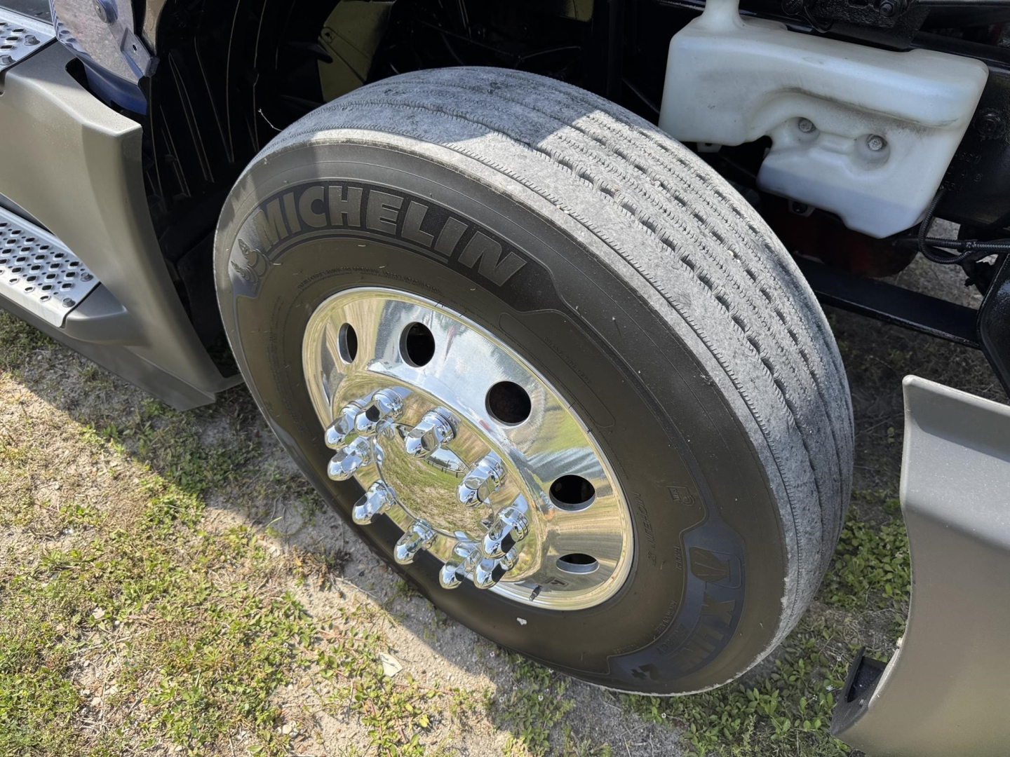 Truck wheel with Michelin tire, polished chrome hub, and part of white plastic reservoir visible in engine bay.