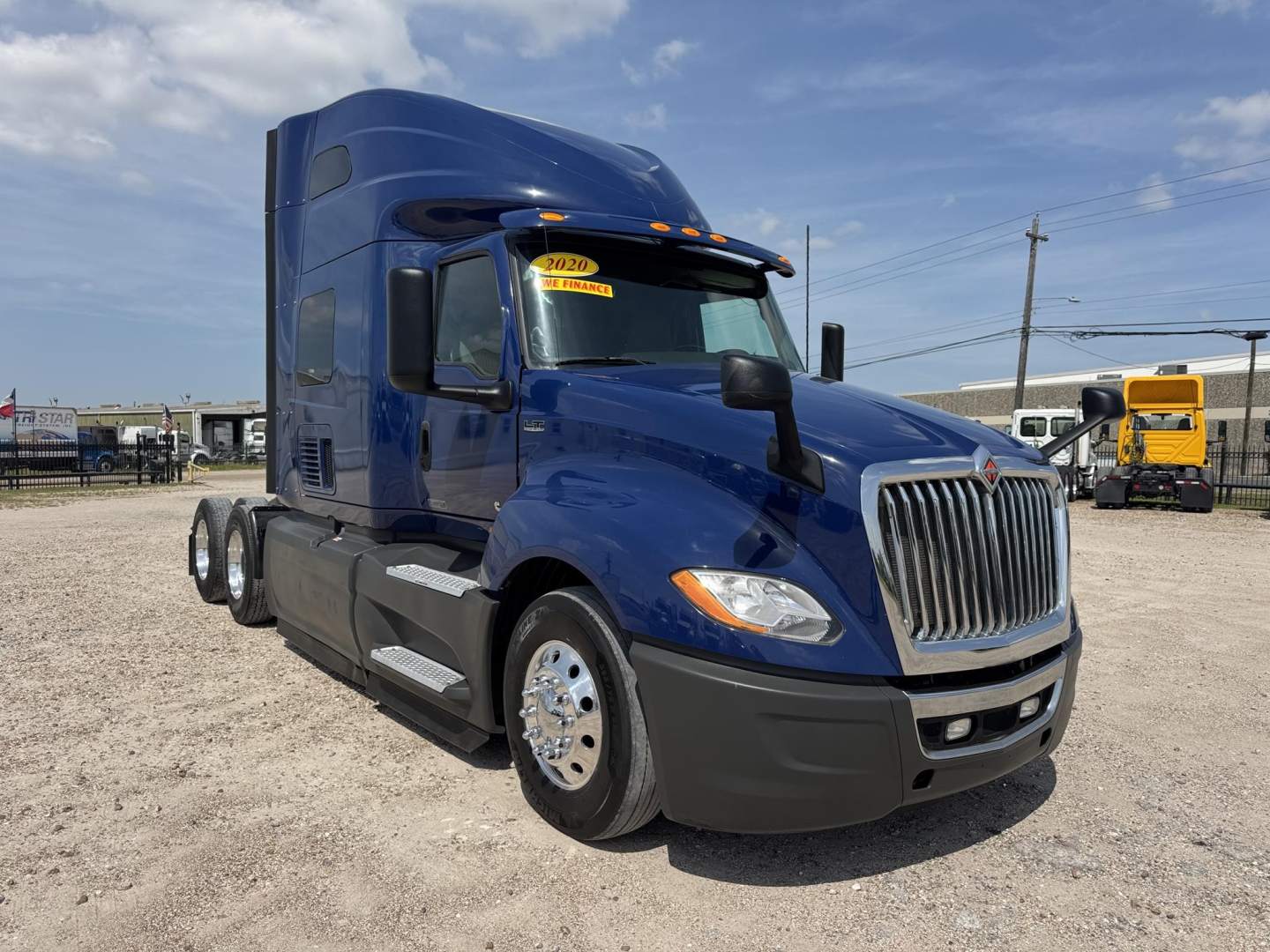 2020 International LT truck in blue, front-right view with sleeper cab and chrome grille. visible stickers on windshield, side steps, fuel tanks, and dual rear axles.