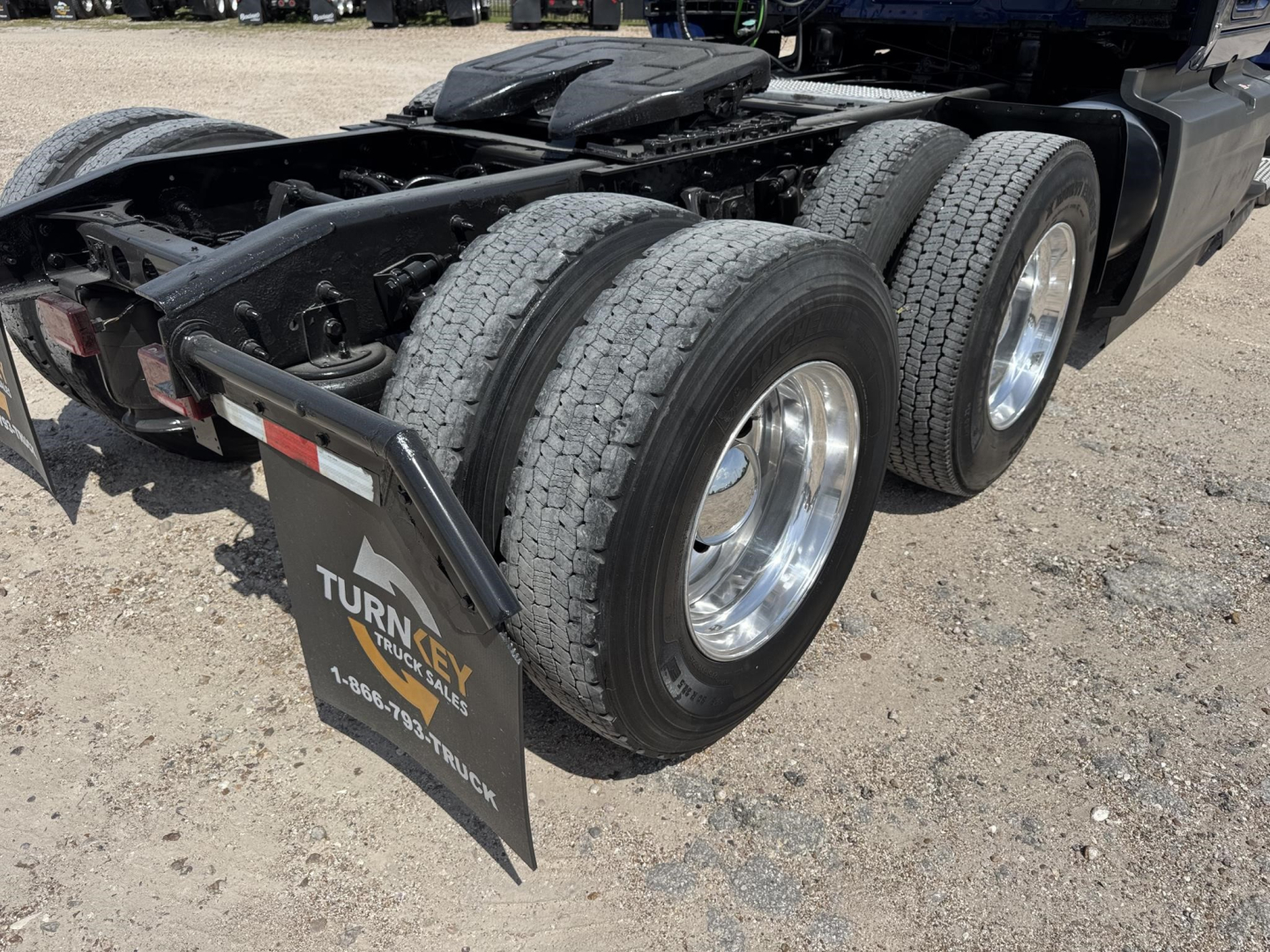 Truck rear with dual rear axles and mudflaps showing Turn-Key Parts & Service logo; tires and chassis visible; gravel lot.