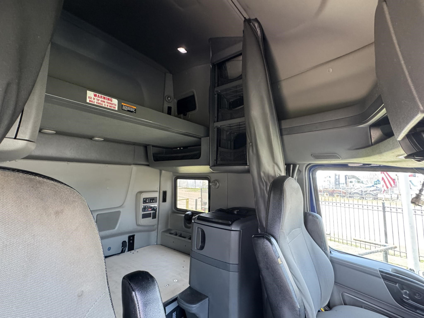 Interior of a 2020 International LT sleeper cab showing bunk area, driver seat, passenger seat, and overhead storage with warning labels.