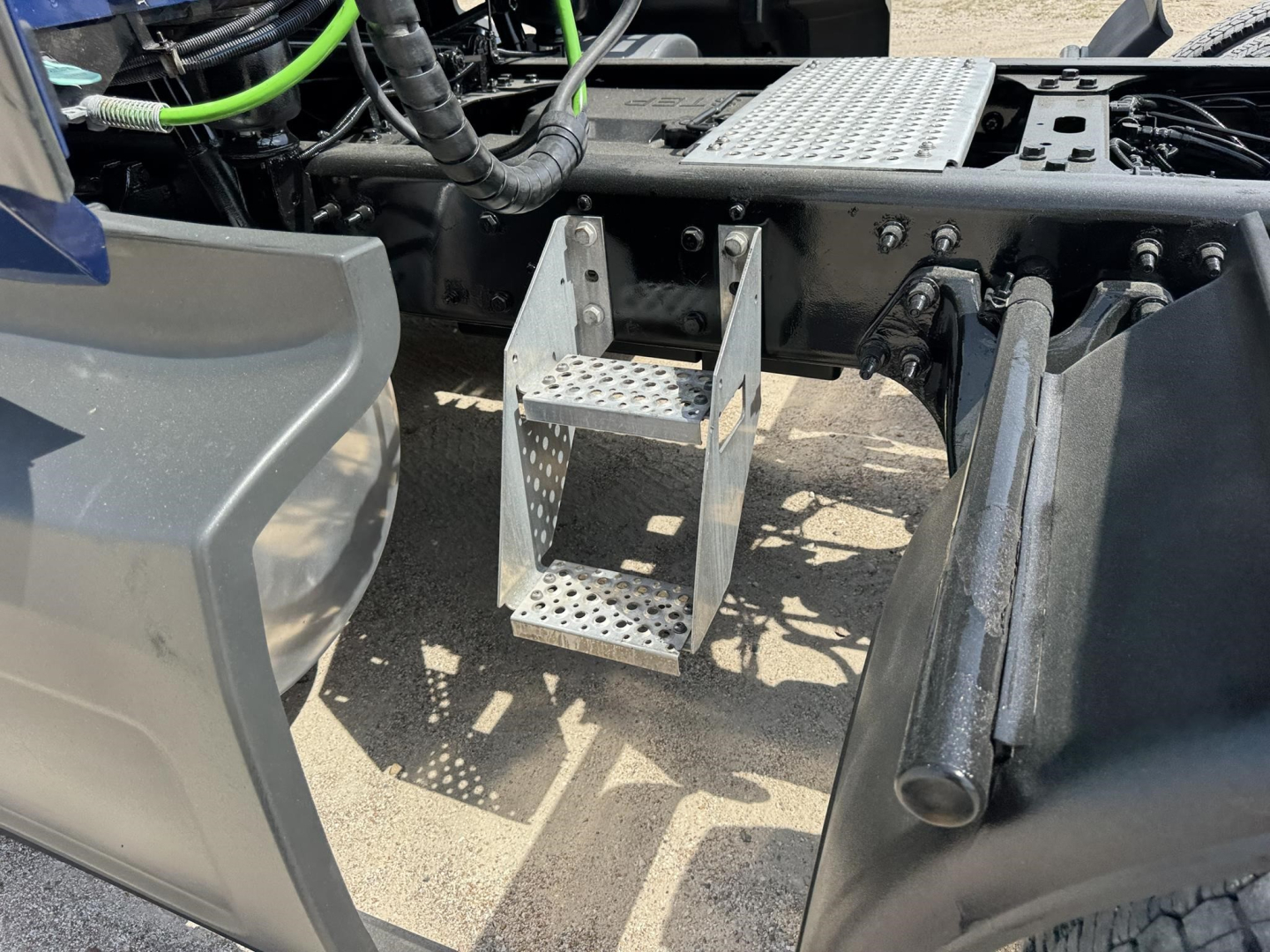 Truck chassis area showing aluminum diamond-plate step brackets mounted to the frame with surrounding components and hoses visible.