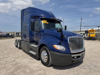 2020 International LT truck in blue, front-right view with sleeper cab and chrome grille. visible stickers on windshield, side steps, fuel tanks, and dual rear axles.