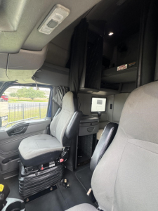 Cab interior of a 2020 International LT truck showing driver seat, passenger seat, overhead sleeper area with storage cabinets, and dashboard elements.