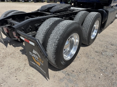 Truck rear with dual rear axles and mudflaps showing Turn-Key Parts & Service logo; tires and chassis visible; gravel lot.