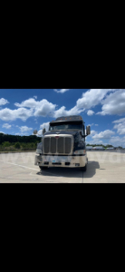 Peterbilt 387 truck front view in a parking lot, with grille and bumper visible, clear blue sky with clouds.