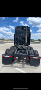 Peterbilt 387 rear view showing fifth wheel/tractor coupling and dual rear axles with tires. Clear sky in background