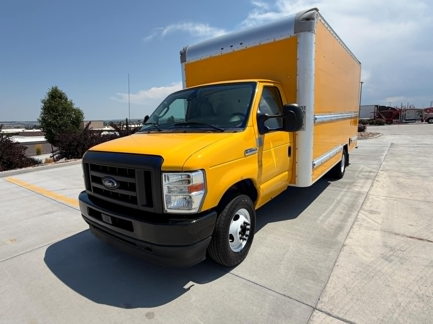Yellow Ford E-350 box truck with a large cargo box, front grille, and side profile visible in a parking lot.