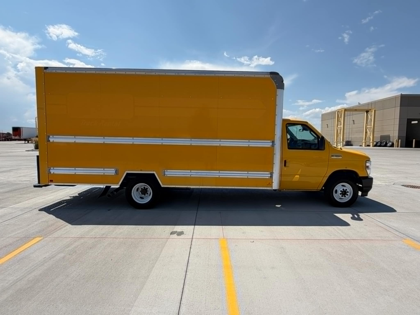 Ford E350 box truck with yellow cargo box and cab, side view showing cargo area and doors, in a parking lot.