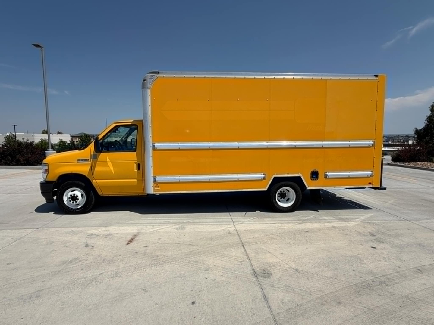 Side view of a bright yellow Ford E-350 box truck with silver trim, no visible text on the box; image shows a long rectangular cargo area and front cab.