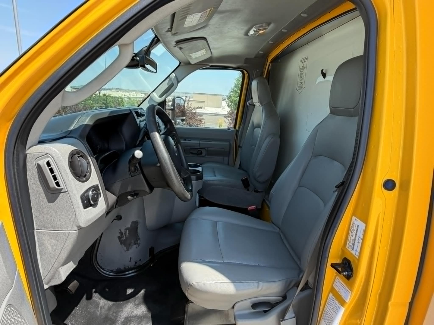 Ford E-350 cargo van interior, driver and passenger seats, steering wheel, dashboard visible through open driver door.