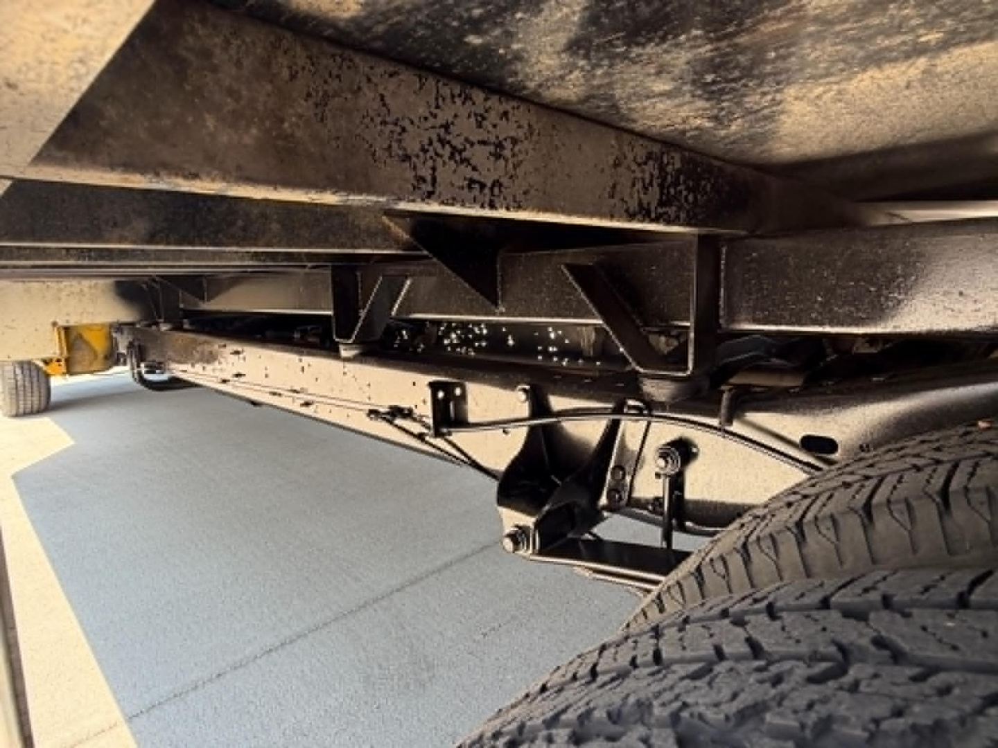 Ford E350 undercarriage showing frame rails, suspension components, and wheel with tire tread from a low-angle view.