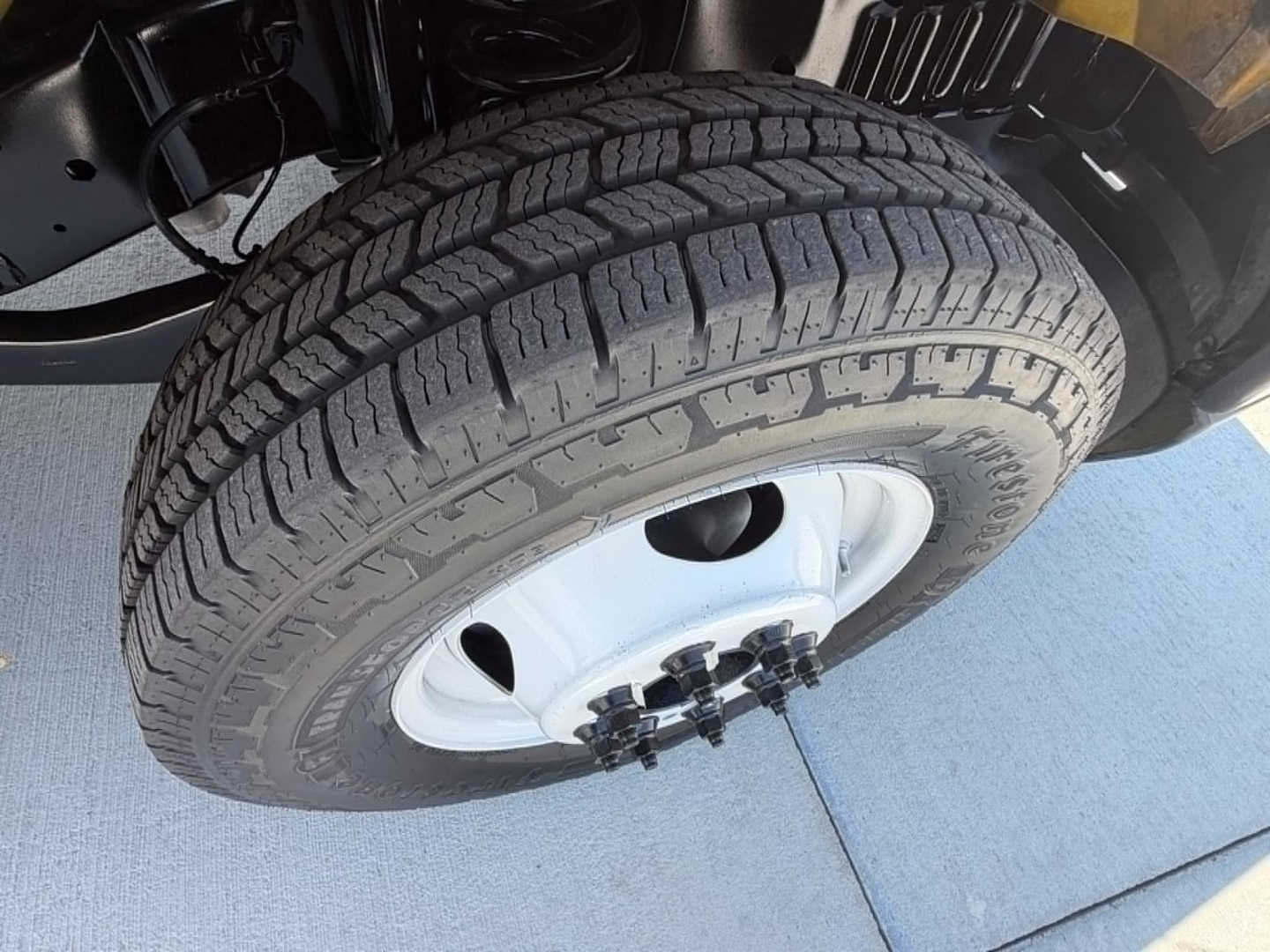 Vehicle wheel and tire close-up on a Ford E350 cutaway truck showing all-terrain tire tread and white steel wheel, front suspension components visible.