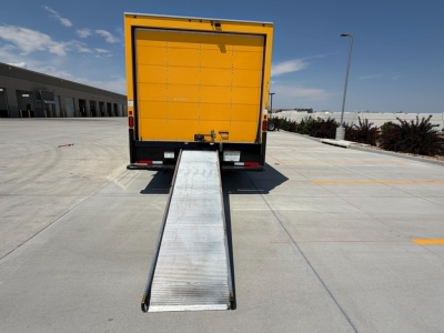Rear view of a yellow Ford E350 box truck with a deployable metal ramp extending to the ground.