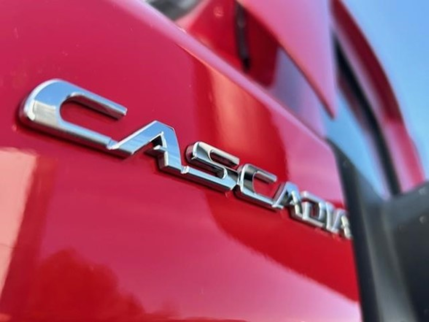 Freightliner Cascadia 126 badge on red truck side, close-up view showing Cascadia chrome lettering.