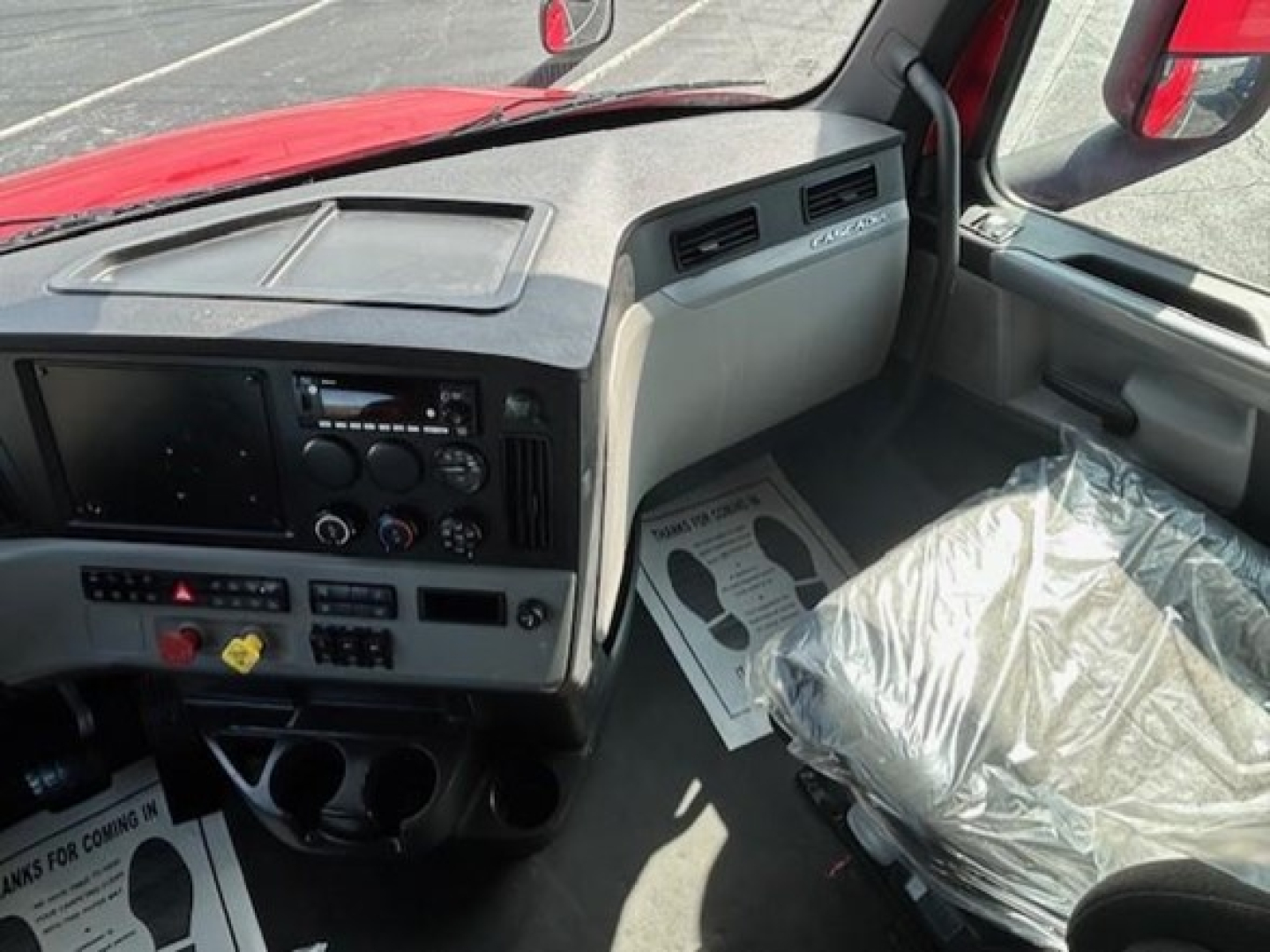 Truck cab interior of a 2022 Freightliner Cascadia 126 showing dashboard with radios and controls, driver seat wrapped in plastic.