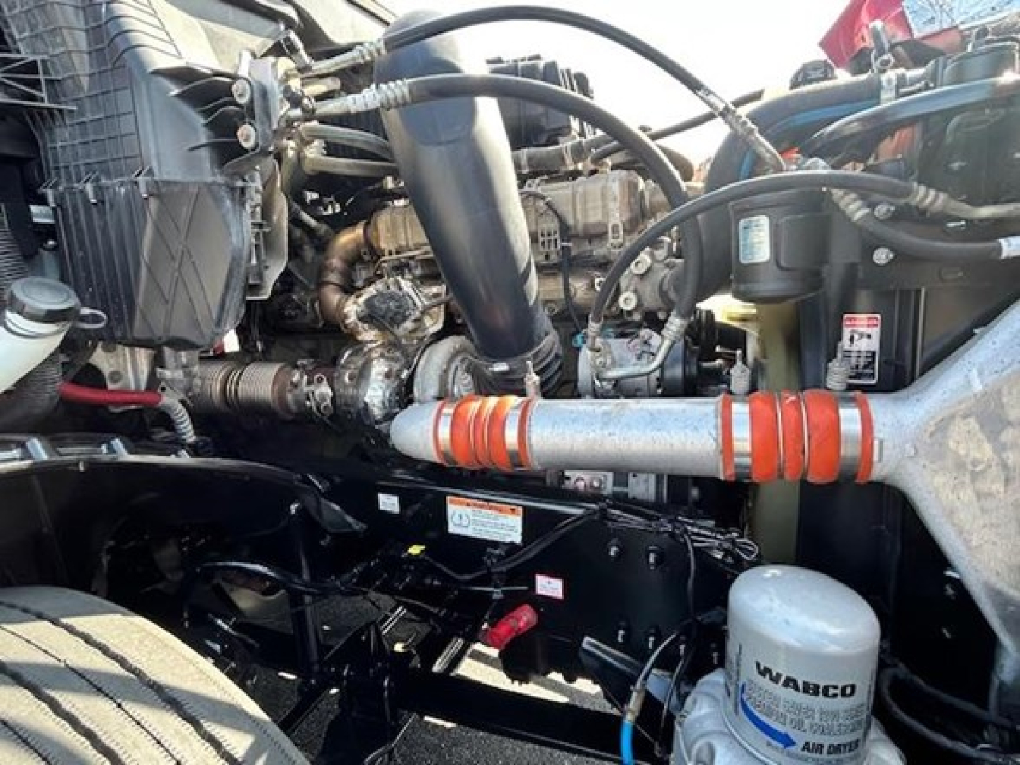 Engine bay of a 2022 Freightliner Cascadia 126 showing hoses, intercooler, and WABCO air filter; visible components include coolant reservoir and various hydraulic lines.
