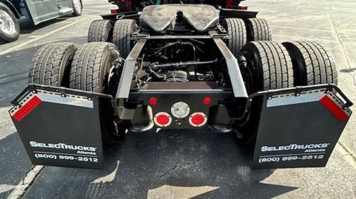 View of a Freightliner Cascadia 126 rear chassis showing dual rear axles with mud flaps and fifth-wheel area, stock number plate, and rear lights.