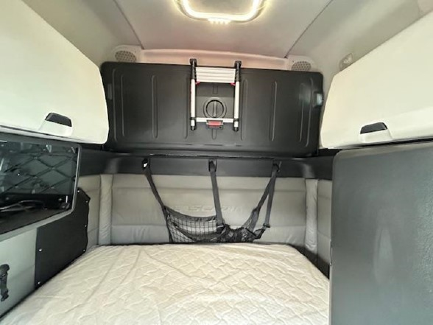 Freightliner Cascadia truck cab sleeper interior showing bunk bed with storage compartments and netting.