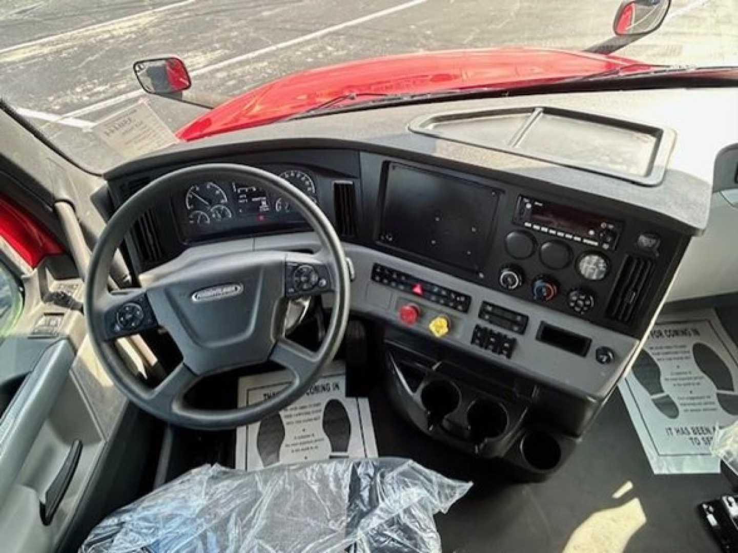Cab interior of a Freightliner Cascadia showing steering wheel, dashboard with gauges, center console, and control panel.