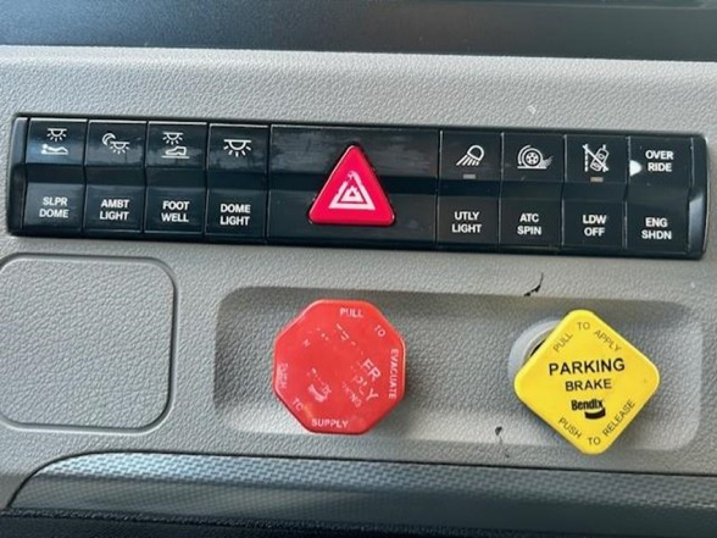 Freightliner-Cascadia dash panel showing hazard button and red engine start/stop and parking brake yellow knob.