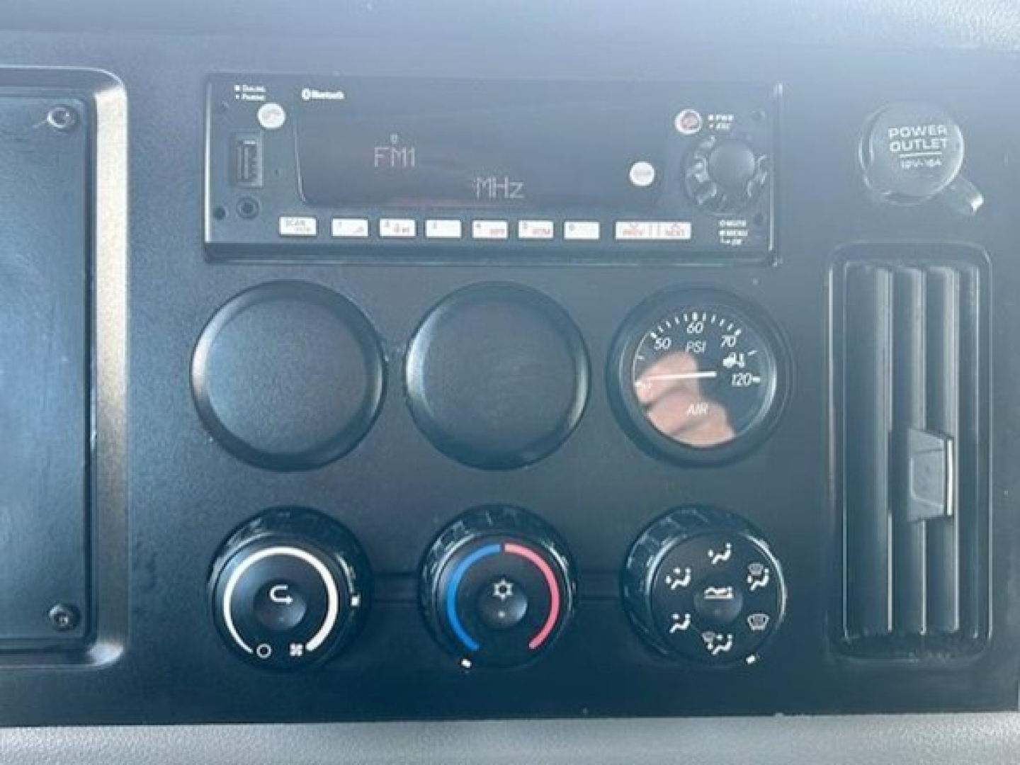 Freightliner Cascadia dash showing radio/CD player labeled FM1 MHz, air gauge, climate controls, and power outlet cover.