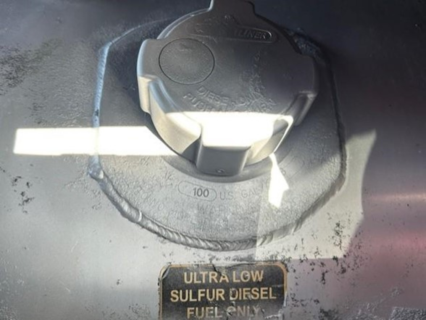 Fuel cap area showing Ultra Low Sulfur Diesel cap with warning label nearby; circular cap with textured edges; surrounding surface with dirt