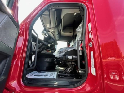 Truck cab interior of a red 2022 Freightliner Cascadia 126, driver seat and dashboard visible from open door, plastic seat cover, steering wheel, and floor mats.