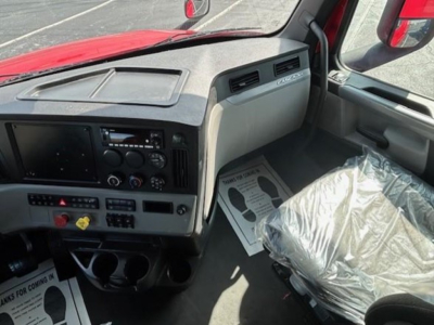 Truck cab interior of a 2022 Freightliner Cascadia 126 showing dashboard with radios and controls, driver seat wrapped in plastic.