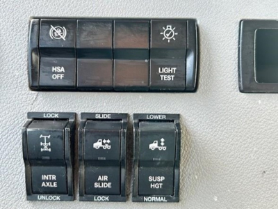 Dashboard switches and controls in a 2022 Freightliner Cascadia 126 showing lighting/test, HSA OFF, INTR AXLE, AIR SLIDE, SUSP HGT, LOCK, SLIDE, LOWER and related icons.