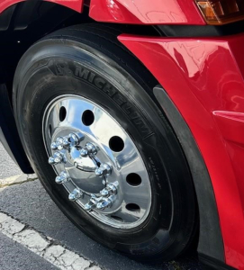 Truck wheel close-up showing Michelin tire and polished chrome hubcap on a red Freightliner Cascadia 126.