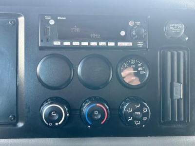 Freightliner Cascadia dash showing radio/CD player labeled FM1 MHz, air gauge, climate controls, and power outlet cover.