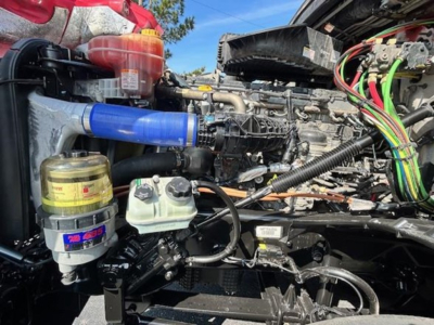 Truck engine bay with blue coolant hose, yellow oil catch bottle, white coolant reservoir, and bundled multi-colored wires visible.