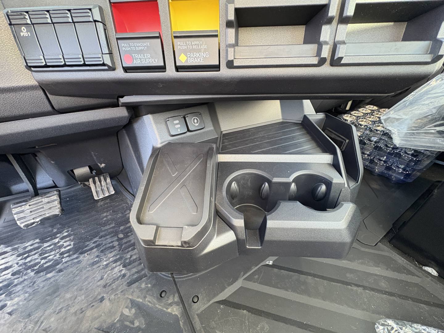 Dashboard area of a new 2027 Mack AN64T daycab showing ignition switches, cup holders, and storage compartments.