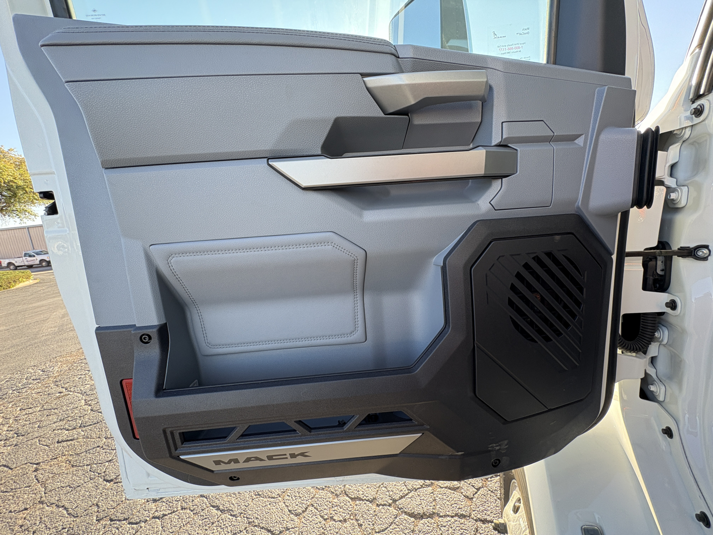 Interior driver door panel of 2027 Mack AN64T cab showing armrest, handle, speaker, and textured panels.