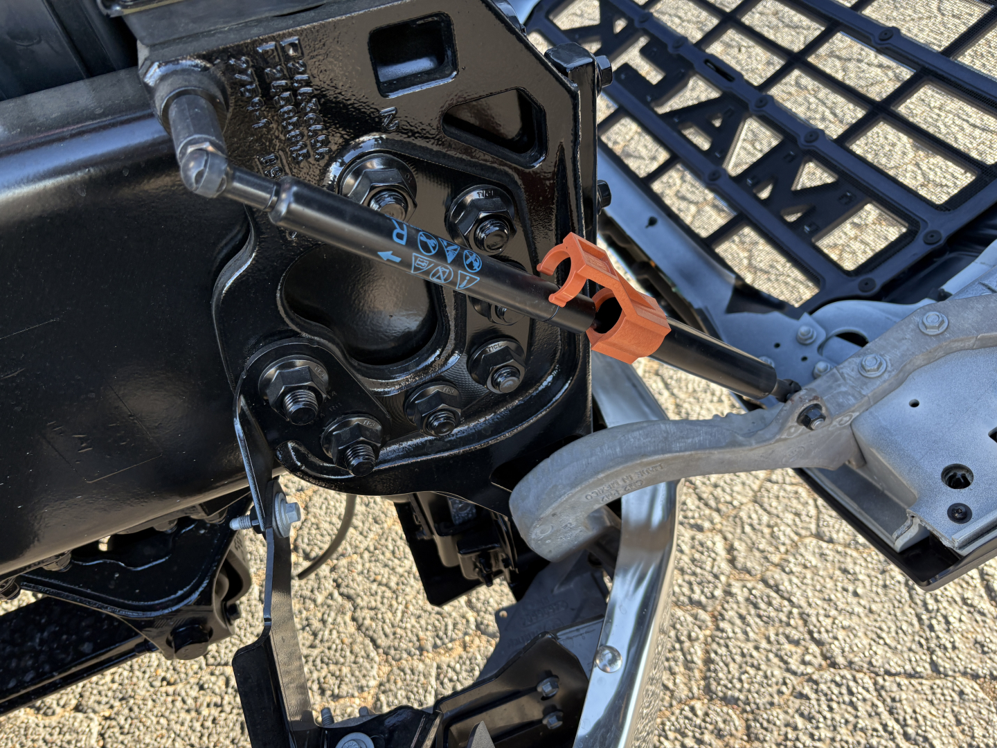 Truck chassis hitch and electrical harness near kingpin area; metal brackets and pins visible; hydraulic lines and wiring loom connected to a towing hitch assembly.