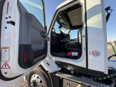 Cab interior of a 2027 Mack AN64T truck seen through open driver door with steps and dashboard visible.