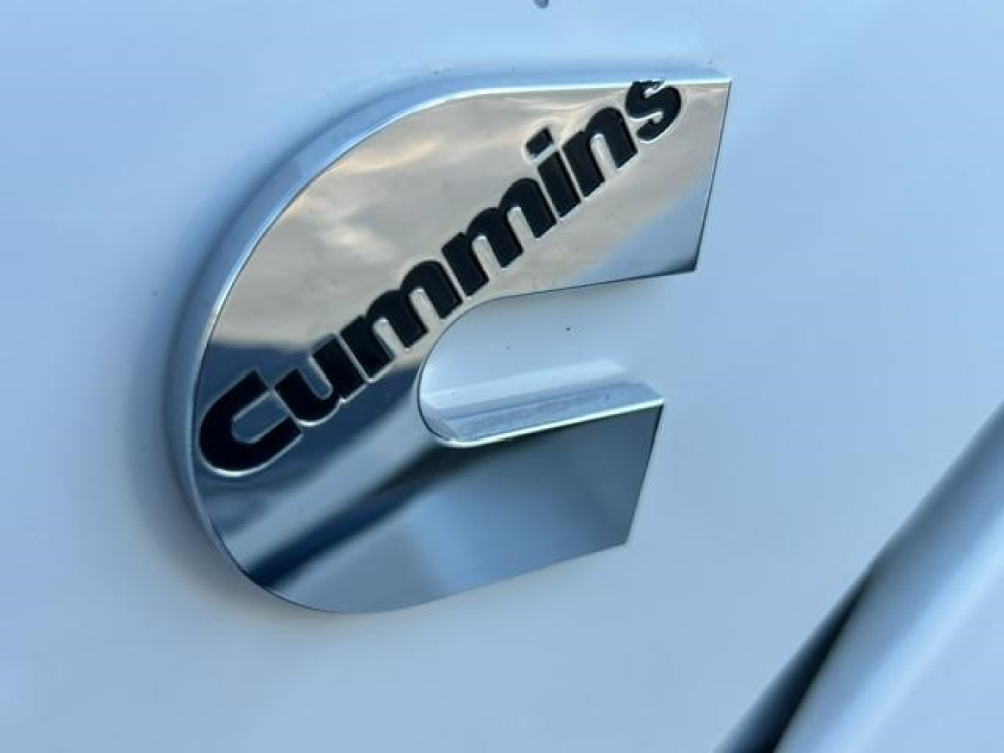 Cummins emblem on side of truck door with chrome finish and light blue paint.