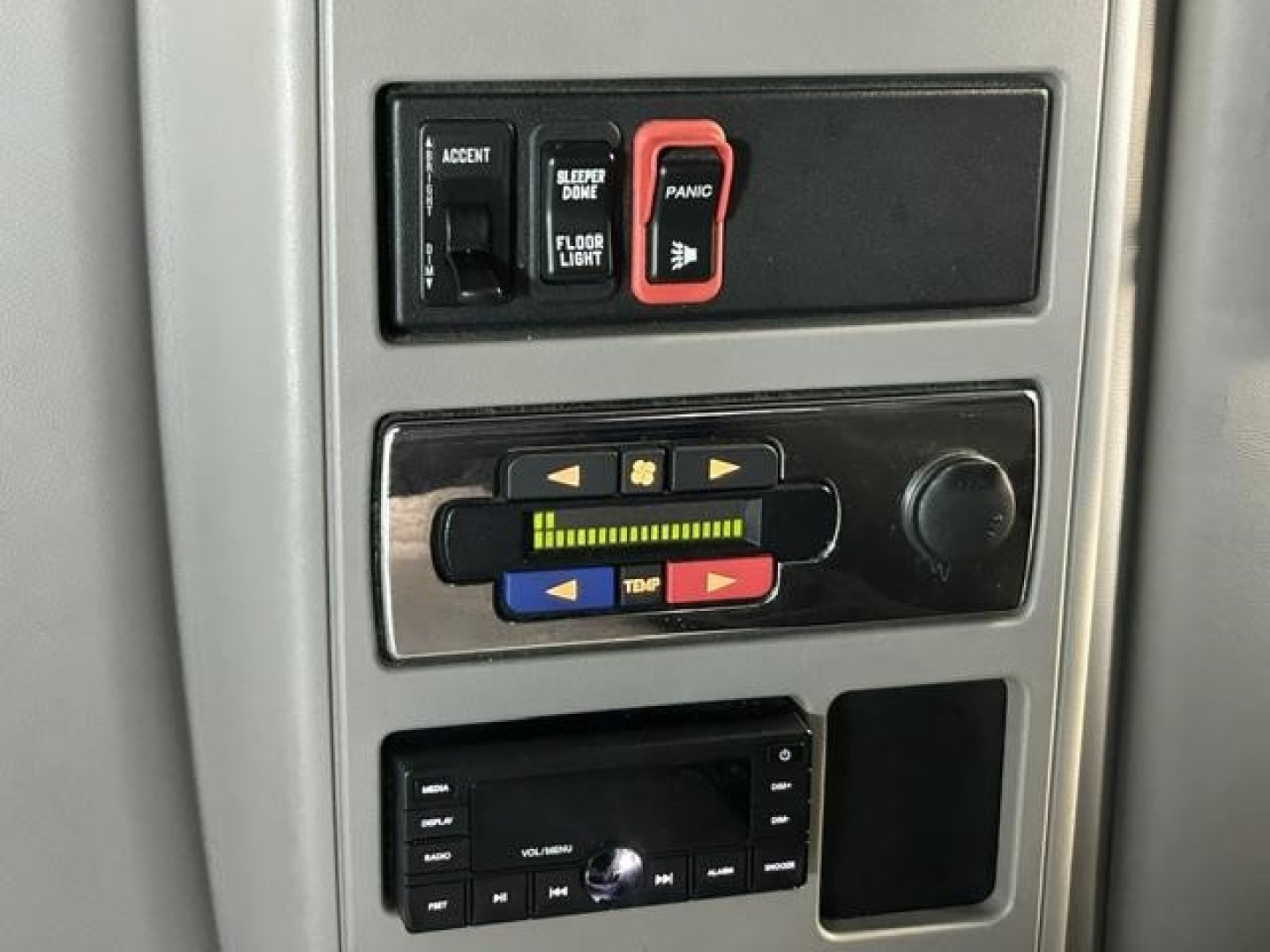 Truck interior switch panel showing Accent and Panik/panic? switches, floor light, sleeper done, and a control panel with colored arrow buttons and a knob. A stock radio or media unit is visible below.